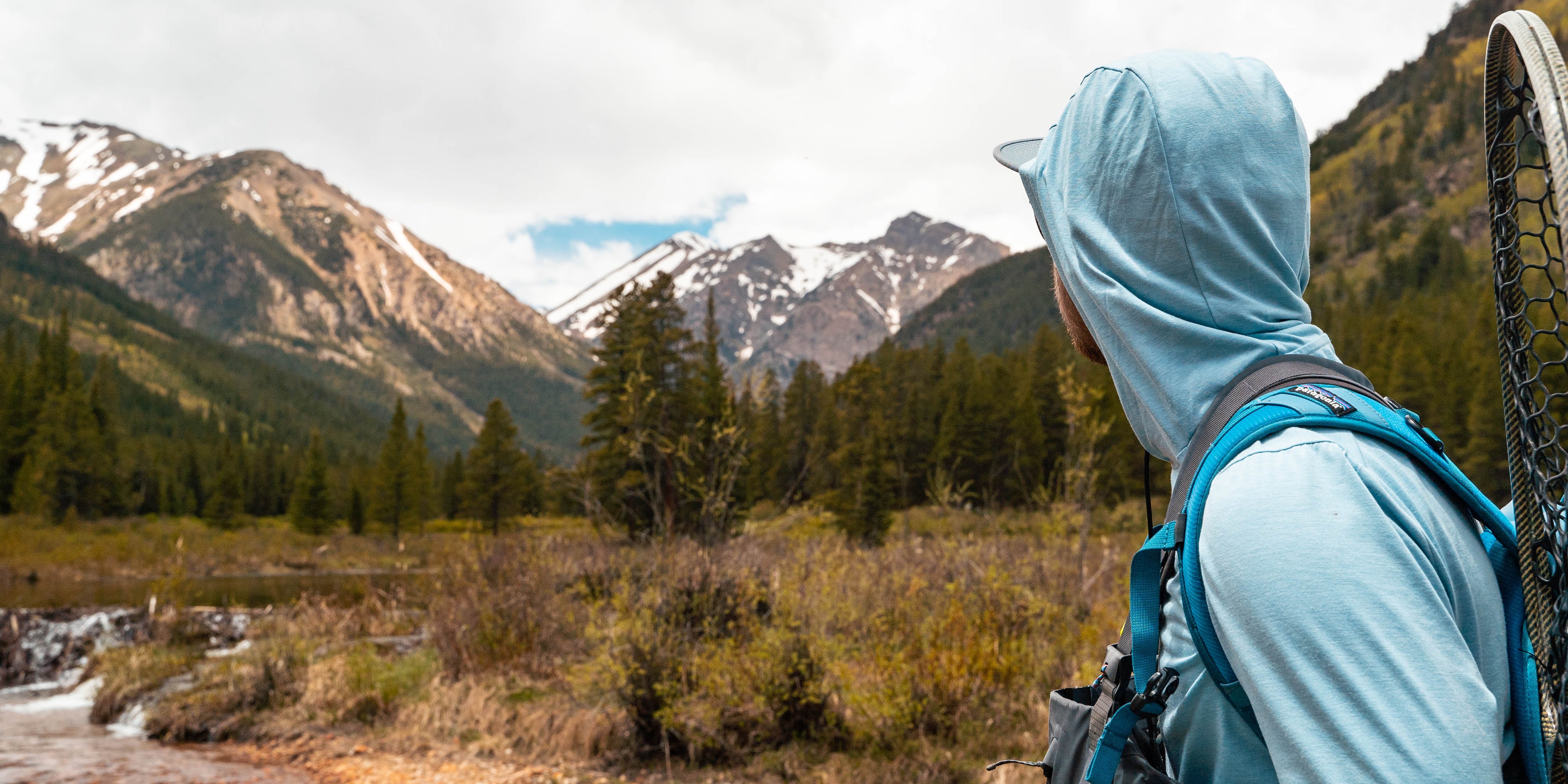 angler looking up stream with mountains in the background