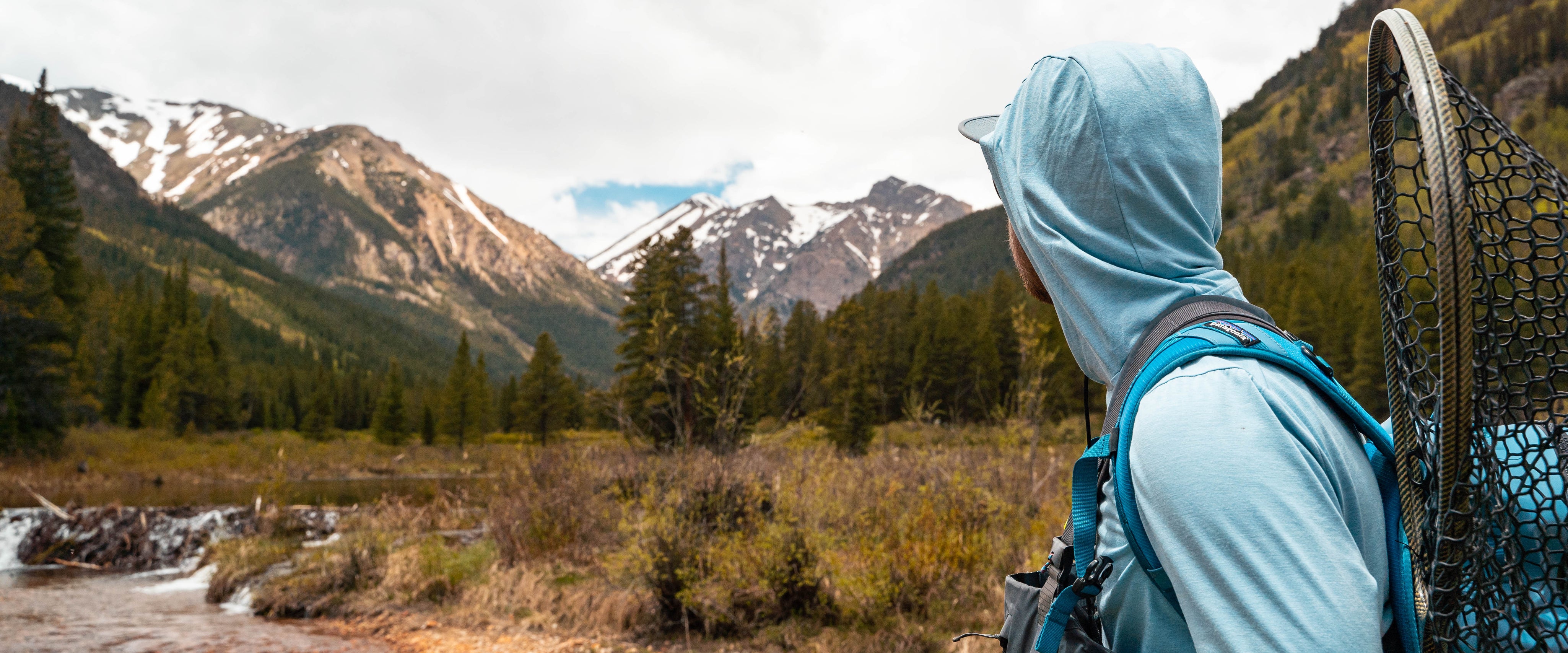angler looking up stream with mountains in the background