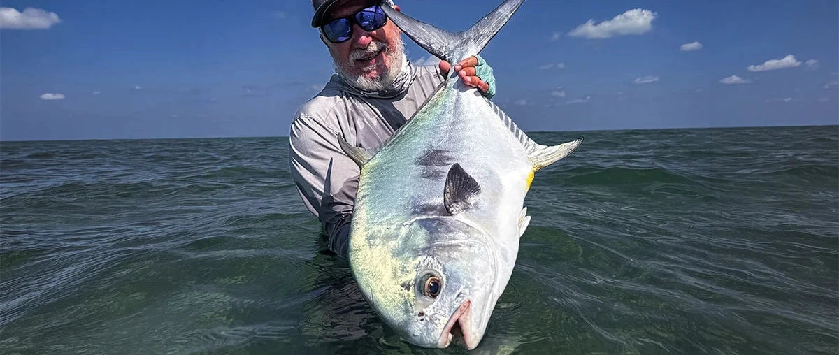 Man holding a large fish in the ocean with a clear blue sky.
