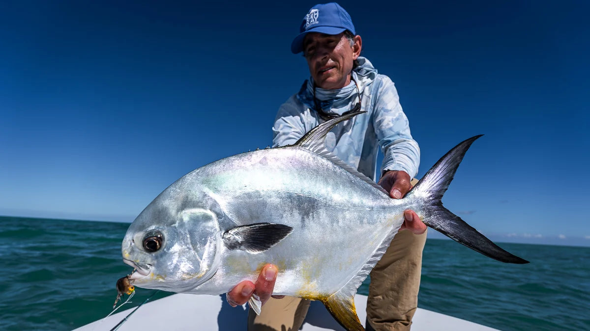 Man holding a large fish on a boat with clear blue sky and water in the background