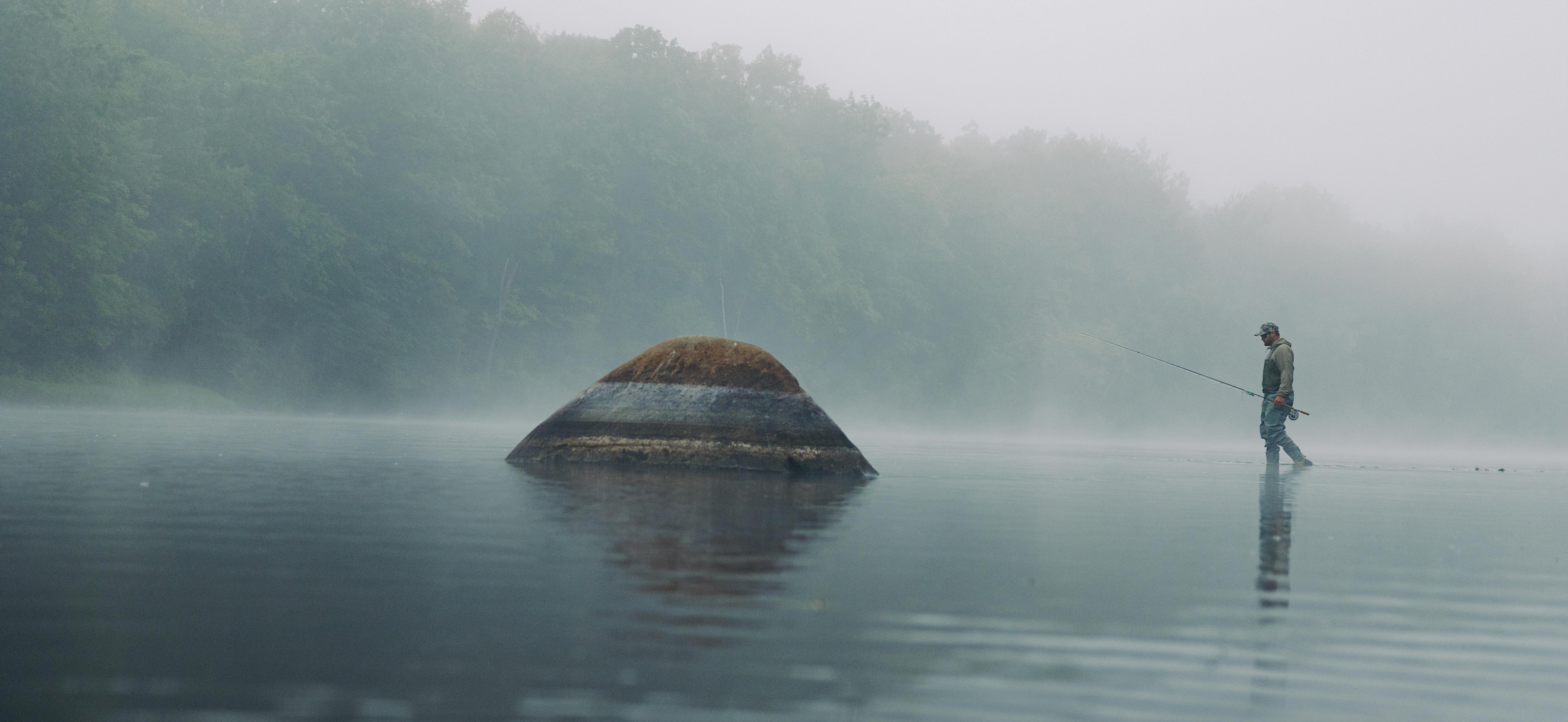 Person fishing on a misty lake with a small island in the background